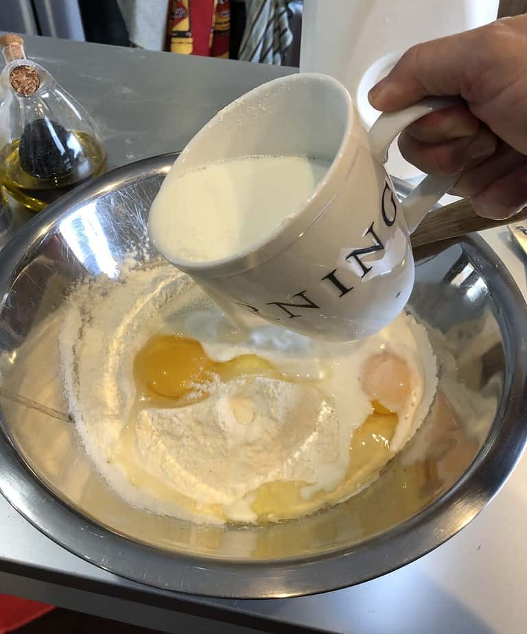 Pouring Milk into a bowl with eggs and flour ready for the easiest pancakes ever.